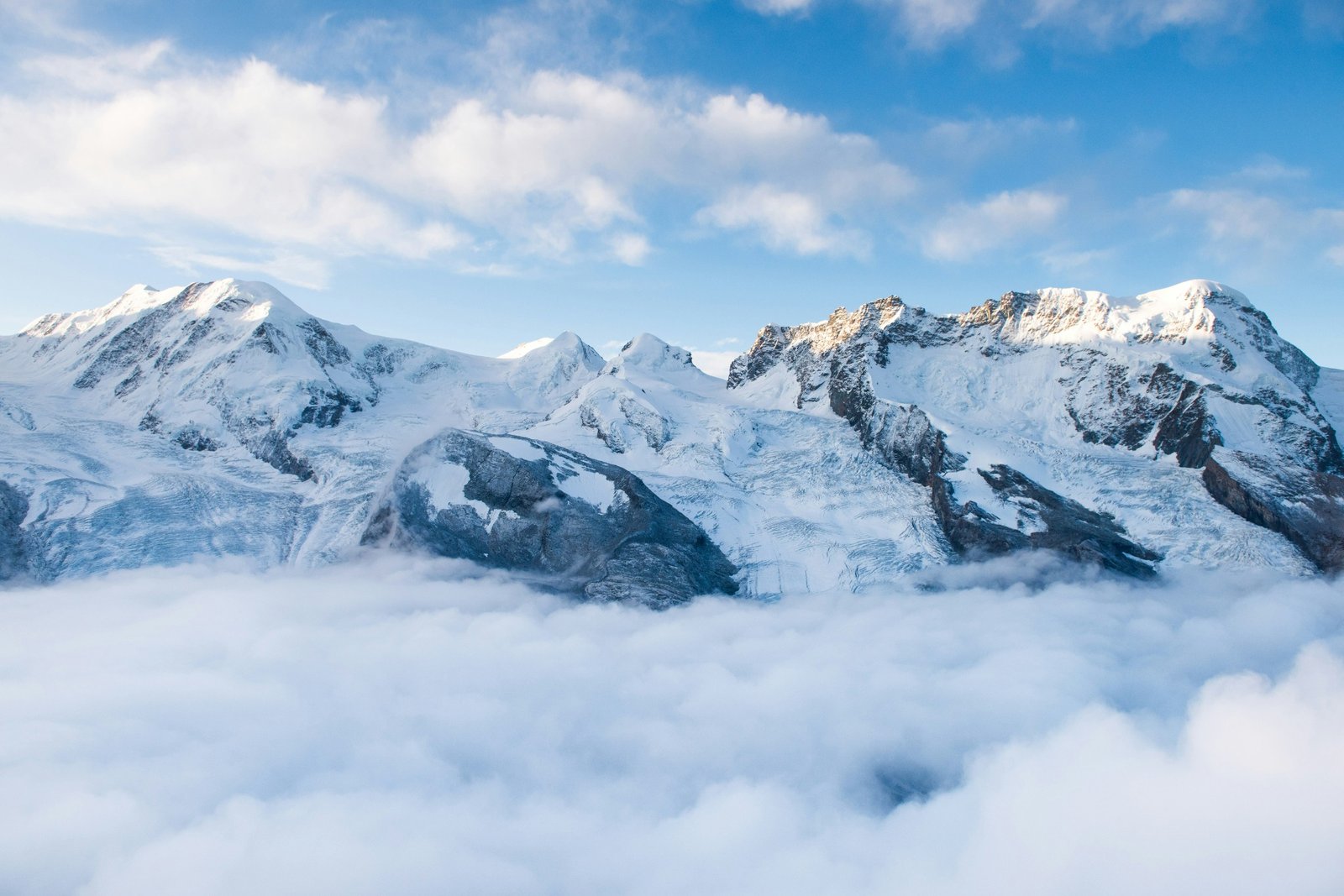Snow-covered alpine peaks above a sea of clouds under a blue sky